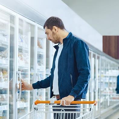 man pushing orange and white shopping cart looking in freezer at grocery store