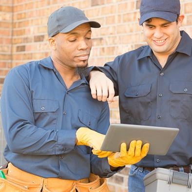 two men in blue standing in front of hvac units and looking at a tablet