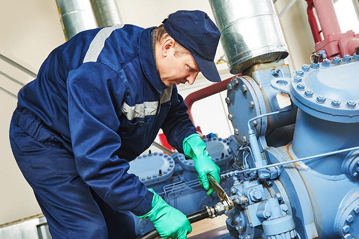 man in blue using wrench on hose attached to machinery