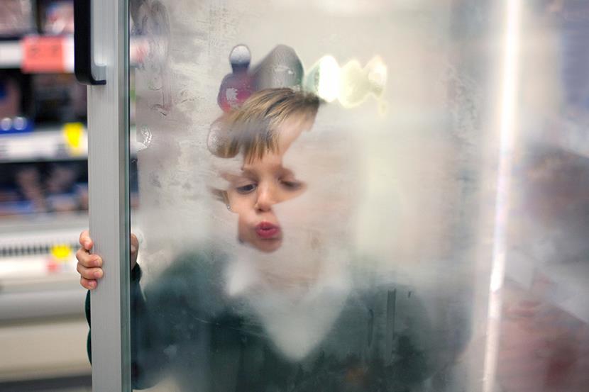 little boy breathing and making designs on open glass freezer door in grocery store