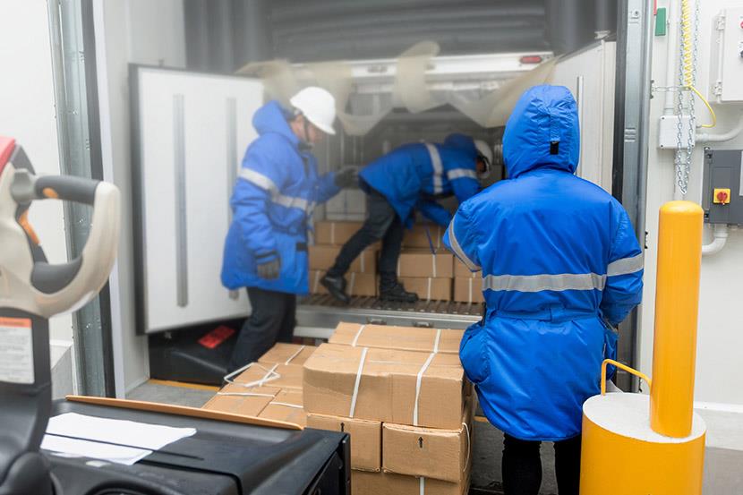 workers in blue jackets unloading boxes of goods from refrigerated truck