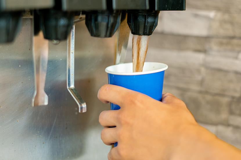 hand holding blue plastic cup against soda machine