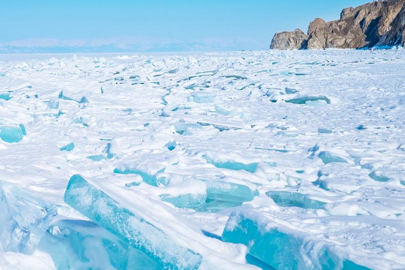 chopped ice floating on frozen lake with rocky cliffs to the right and mountains in the distance
